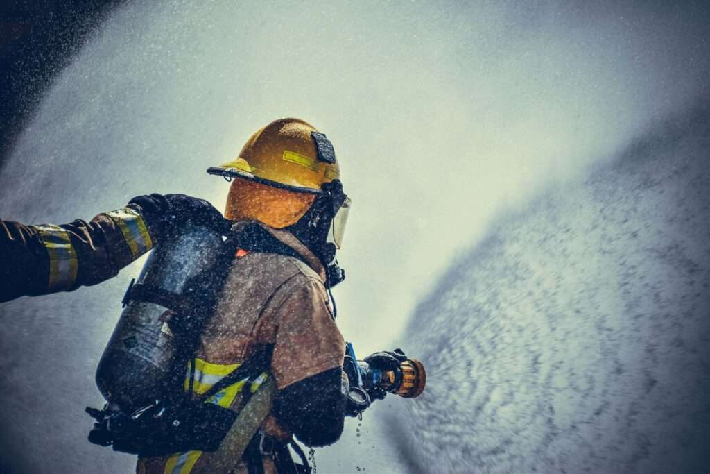 A brave firefighter in protective gear sprays water during training or emergency. A brave firefighter in protective gear sprays water during training or emergency.