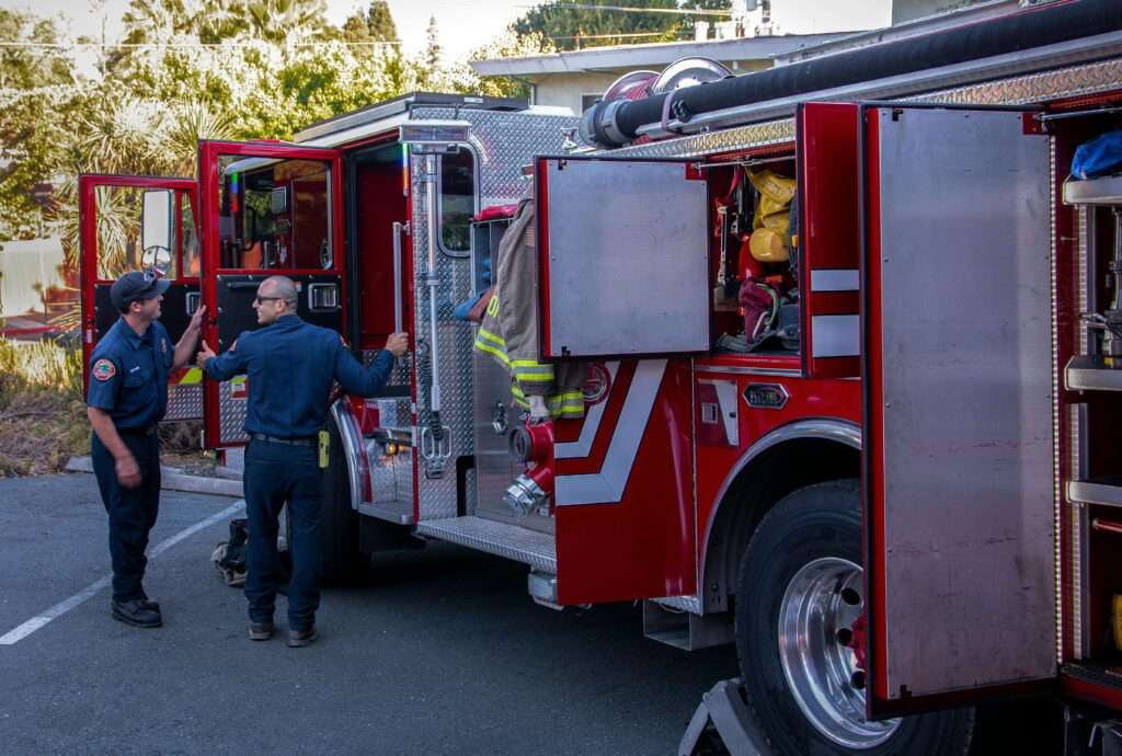 Firefighters inspect and prepare equipment on a fire truck outside the station.